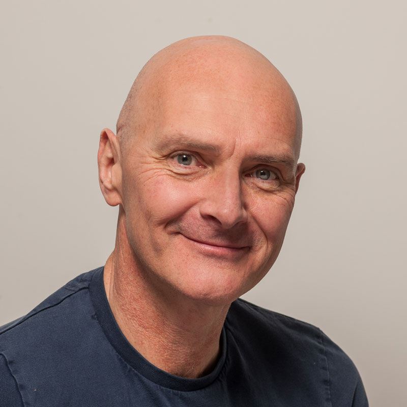 Image of a white, bald man with grey/blue eyes wearing a dark blue t-shirt.