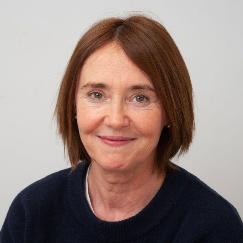Image of a white woman with short auburn straight hair, hazel eyes and a navy blue jumper.