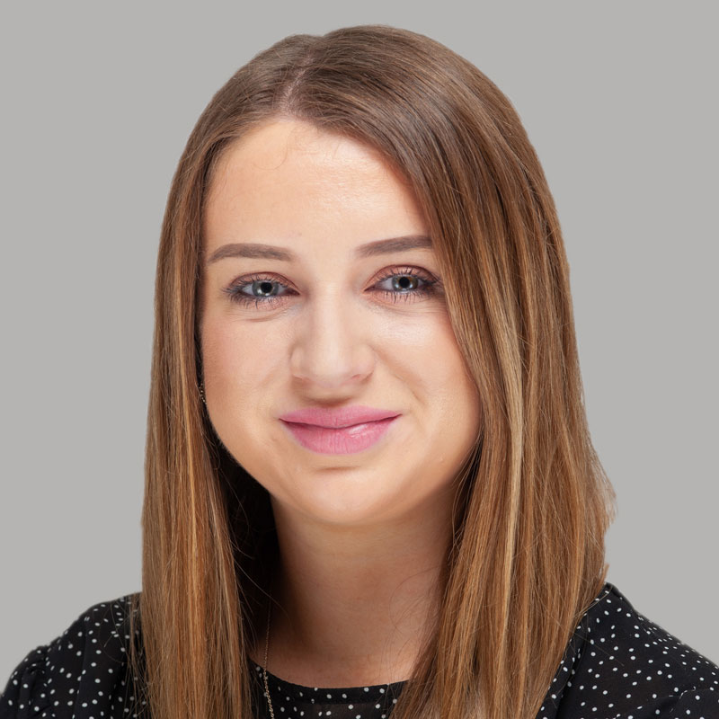 Image of a white woman with brown/blonde long straight hair, blue eyes and is wearing a black top with white polka dots.