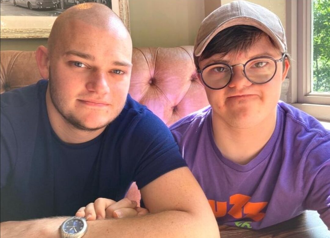 Image of a young man with Downs Syndrome sitting next to another man who is supporting him as a Befriender.