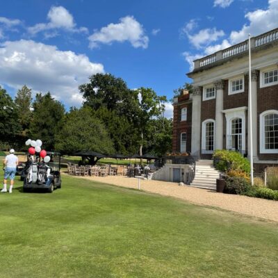 Image of the Richmond Gold Club clubhouse. In front of the building is a golf cart with white and red balloons tied to the back of it.