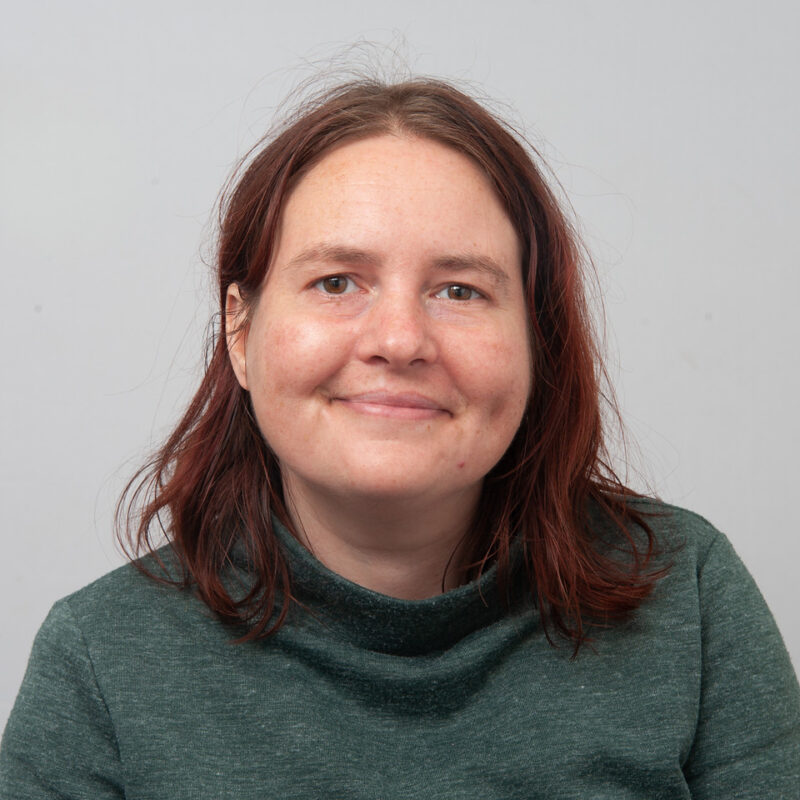 Image of a white woman with brown eyes and red/brown hair wearing a dark green turtle neck shirt.