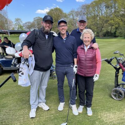 Three men and one woman participating in the Ruils golf day. They are standing on the course and holding their clubs.