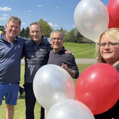 Four Ruils golf day participants standing out on the gold course. A woman is holding red and white balloons being used for the mulligans.