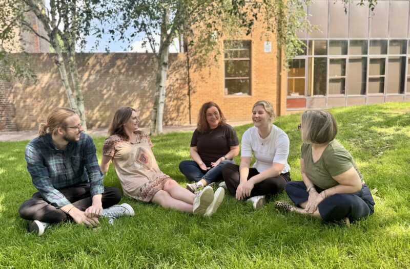 Five members of the Ruils team seated on a grassy lawn having a chat.