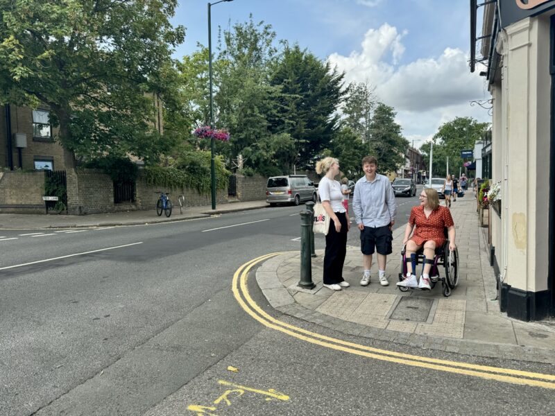 Three women walking down the high street. One is a wheelchair user and the other two are walking. There are blue skies in the background.