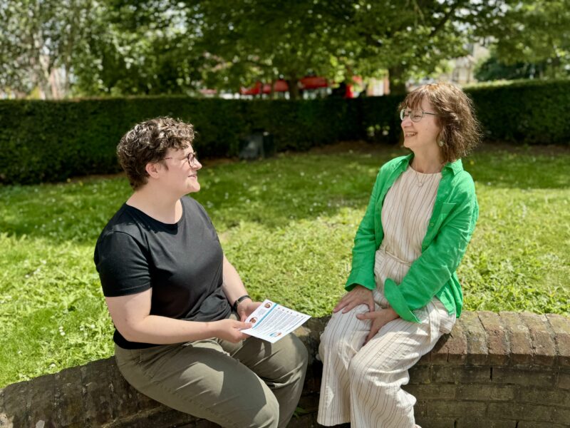 Two women sitting on a brick wall having a laugh about something.