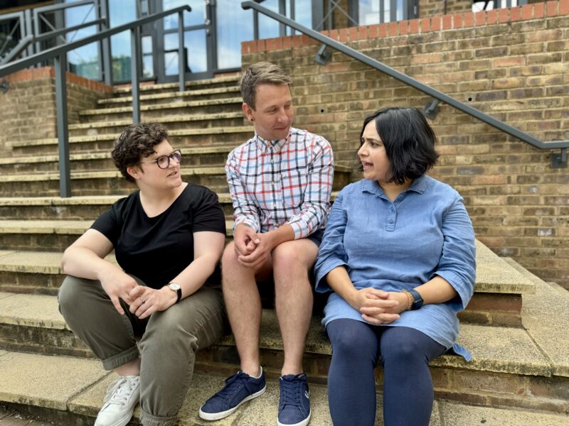 Three members of the Ruils team sitting on steps at the entrance to an office building having a chat.