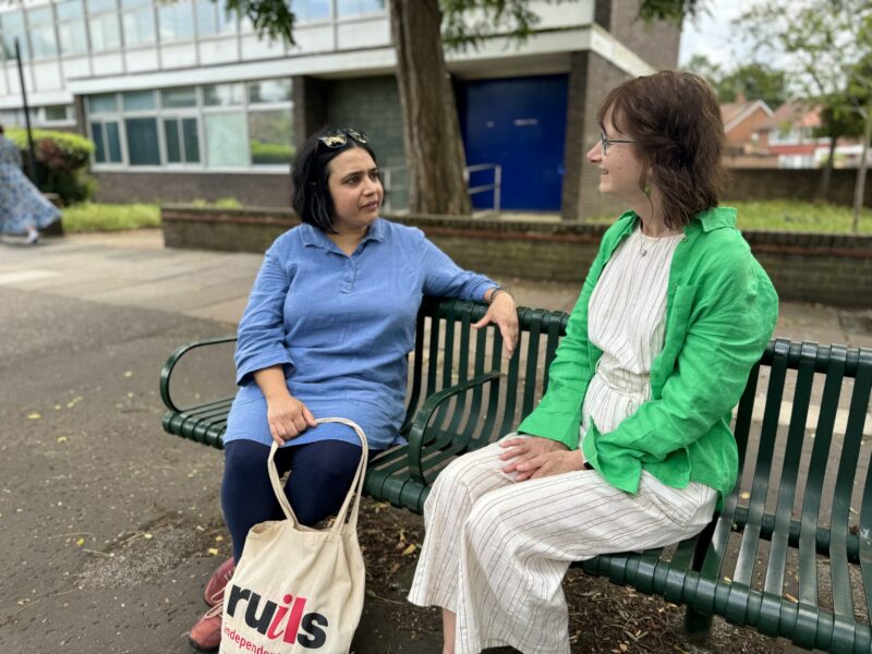 Image of two women sitting on a park bench chatting to each other.