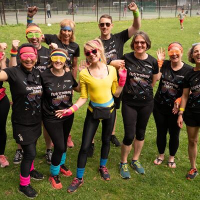 Group photo of the dragon boat race team that competed in Kingston to support rules. They are all wearing black T shirts and the person in the middle is wearing a yellow leotard and black tights. They have their hands in the air celebrating.