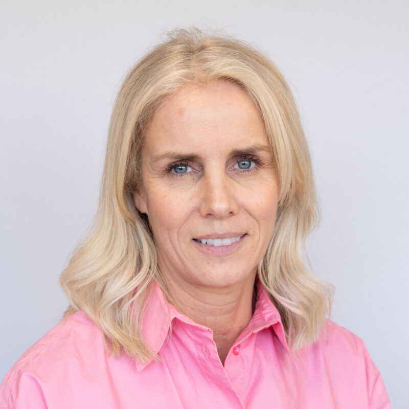 Image of a white woman with blue eyes and light blonde hair wearing a light pink button up shirt.