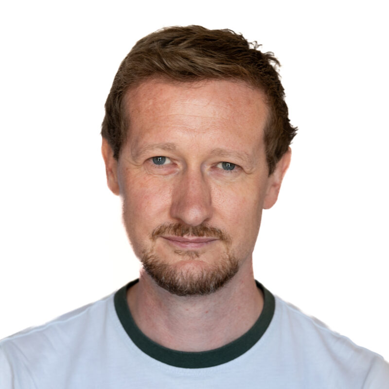 Picture of a white man with short dark hair with a moustache and light beard.