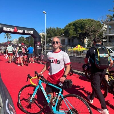 Image of supporter Owen wearing a team Ruils T shirt standing next to his light blue bike after completing an Iron Man challenge event.