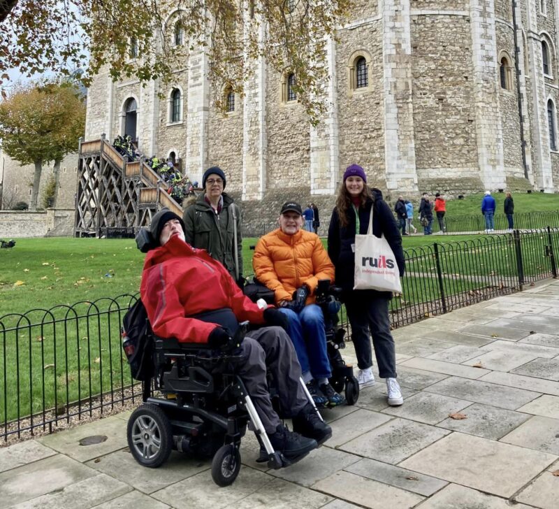 Two men in wheelchairs and two women standing next to them posing in front of the White Tower at the Tower of London.