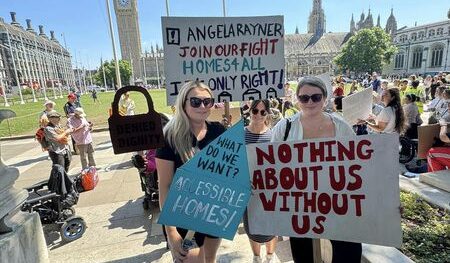 Three women wearing sunglasses holding placards at a protest about accessible housing in parliament square.