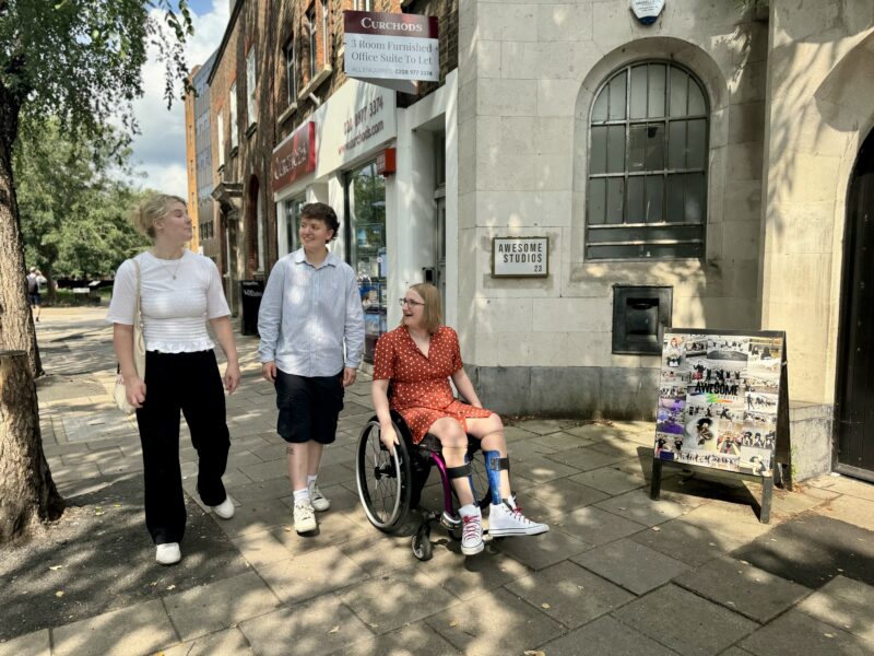 Image of three women walking down the high street. One is a wheelchair user and the others are walking.