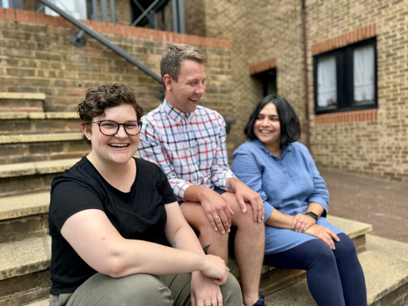 Three members of the Ruils staff team sitting on steps leading up to an office building. They are all laughing.