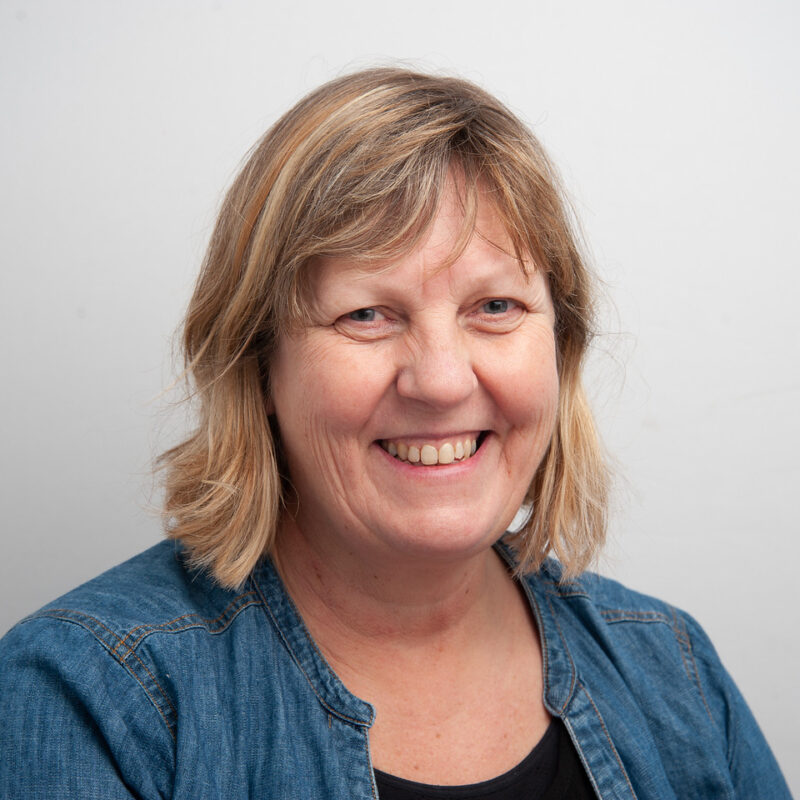 Image of a white woman with medium blonde shoulder length hair and a fringe. She is wearing a jean shirt with a black t-shirt underneath.