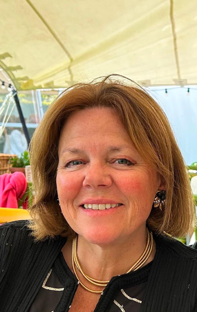 Image of a white woman with tanned skin, light brown shoulder length hair, wearing silver earrings and a black top.