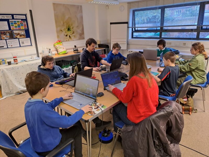 The Ruils Minecraft group members sitting around a group of tables. All are playing the game on their laptops.