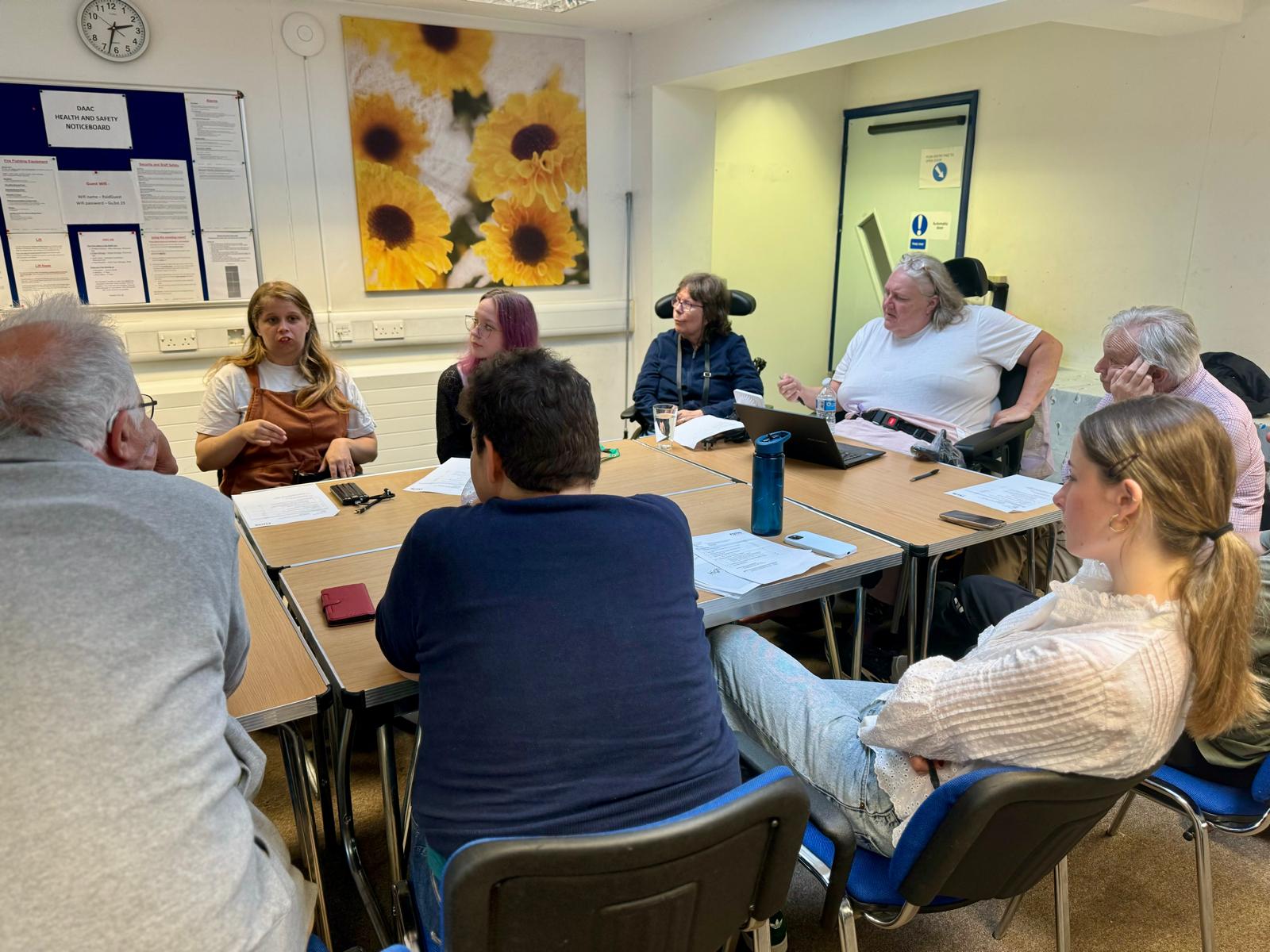 Image of a group of Disabled people sitting around a table in a meeting room having a discussion.