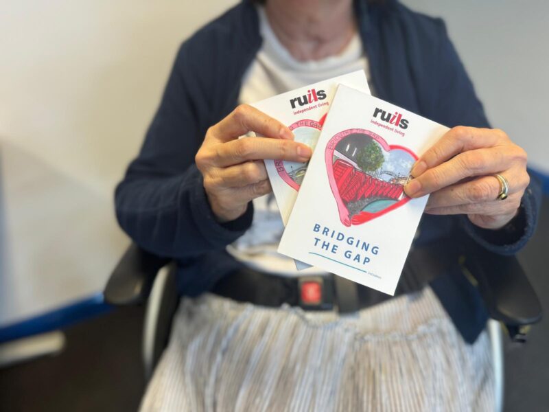 Volunteer Patty holding up the two versions of the Ruils Bridging the Gap mental health booklet.