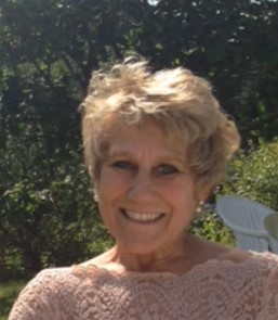 Image of a white woman with short blonde wavy hair wearing a light pink dress.