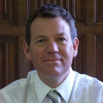 Image of a man with olive skin, dark brown hair who is wearing a white collared shirt and a light green tie.