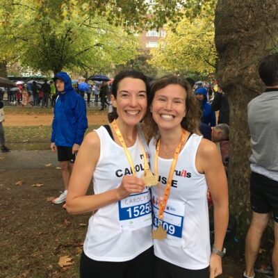Two female runners in Hyde Park holding their Royal Parks Half medals and smiling