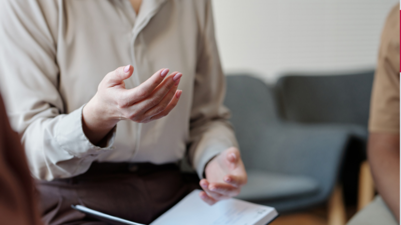 Social Housing drop-in session image, image of a woman sitting at a desk gesturing with her hands