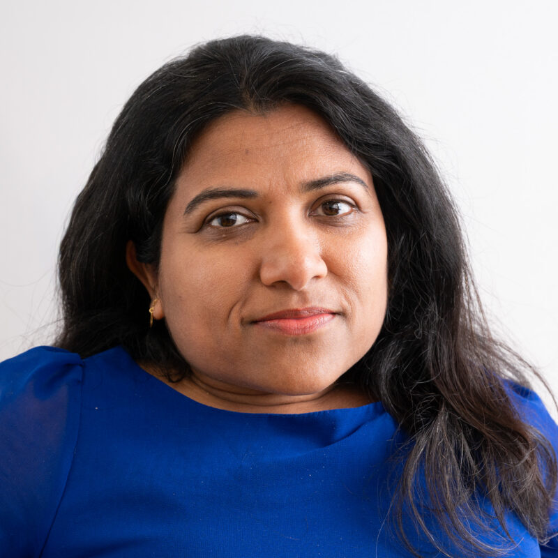 An image of a woman with light brown skin, dark long hair wearing a bright blue top