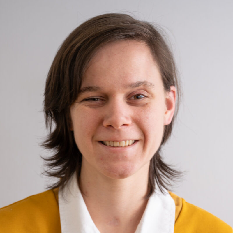 Image of a woman with pale pink skin, light brown shoulder length hair wearing a yellow jumper with a white collar