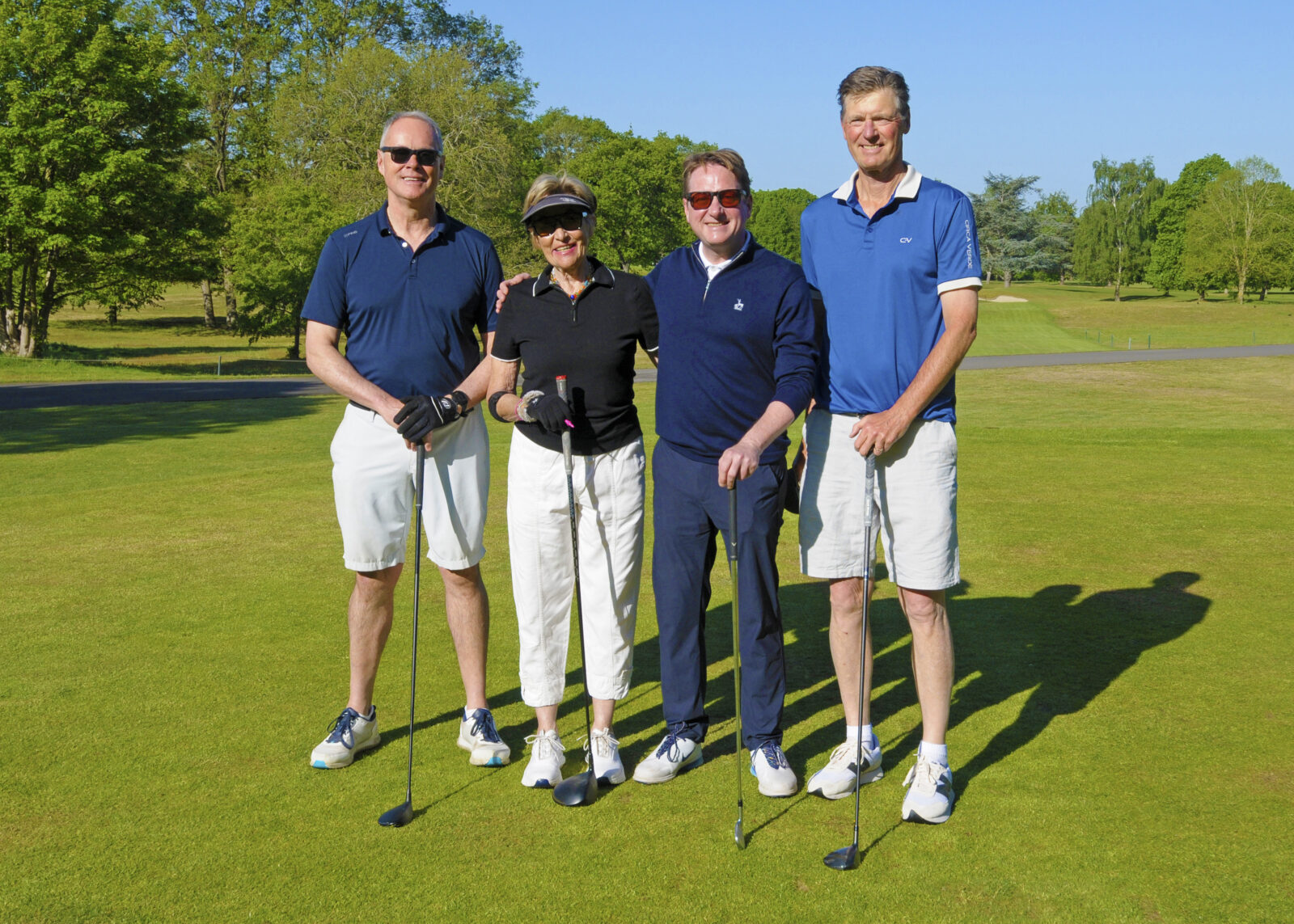 Four players standing on The Richmond Golf Course with their clubs smiling in the sunshine