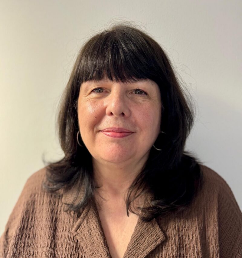 Woman with a fringe and dark shoulder length hair and blue eyes