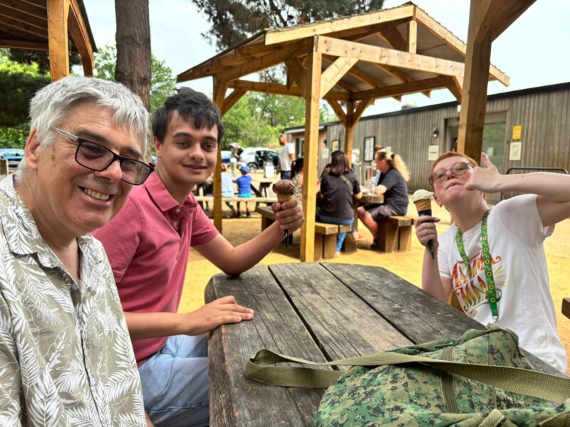 Image of two young people and a carer sitting at a picnic table enjoying an ice cream cone