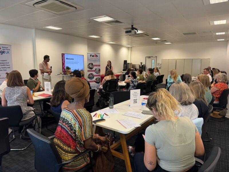 Image of a conference room full of people facing a man and woman who are speaking into microphones, addressing the audience.