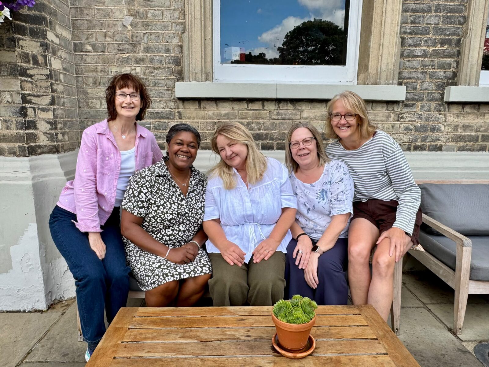 Image of 5 women sitting on an outdoor sofa in front of a brick building