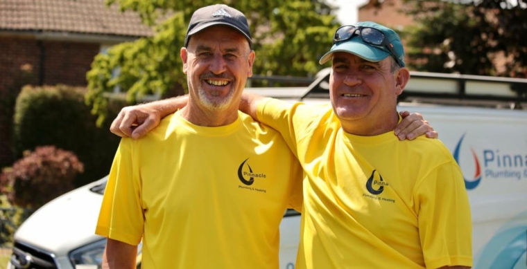 Image of two men wearing matching yellow t-shirts - one has his arm around the other and they are smiling at the camera