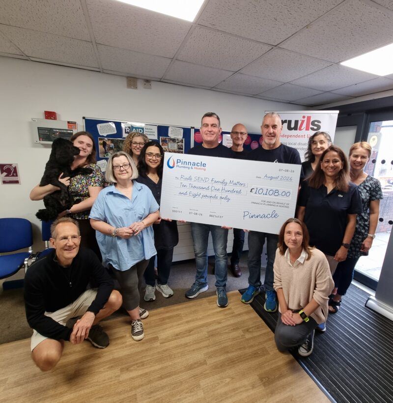 A group of people in an office lobby standing with a large cheque for £10k